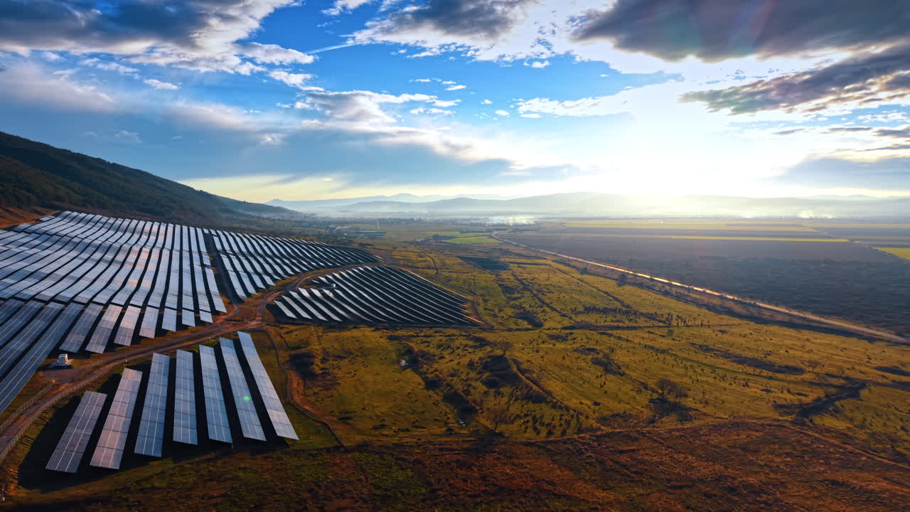 Varmt solnedgangslys over et stort solcelleparkanlæg. Bredt luftfoto af et fotovoltaisk anlæg i en bjergdal under solnedgang med diset atmosfære og gylden belysning.