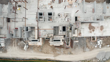 Top-View-Aerial-Flight-Over-New-Commercial-Building-Under-Development-with-Employed-Union-Construction-Site-Workers-Operating-Heavy-Industrial-Machinery-Jobs-Urban-Real-Estate-Housing-Flyover-4K