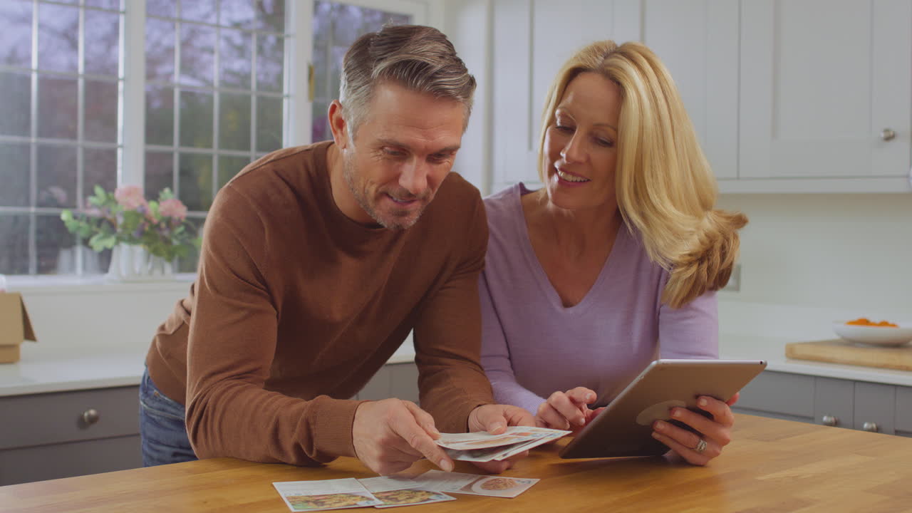 デジタルタブレットを使って一緒にレシピアイデアを研究するキッチンでの成熟したカップル - スローモーションで撮影
