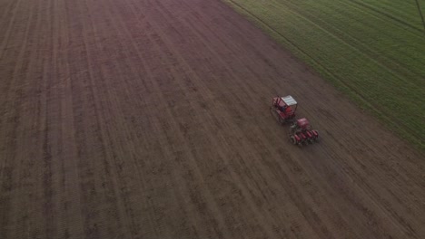 aerial agricultural farming with red tractor plowing the land in scenic hills farm countryside, drone fly above pillar of dust trails behind, preparing soil for planting new crop