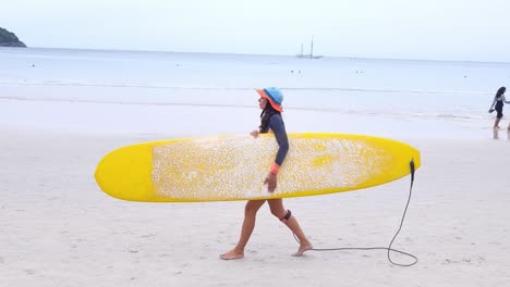 mujer caminando con una tabla de surf en una playa