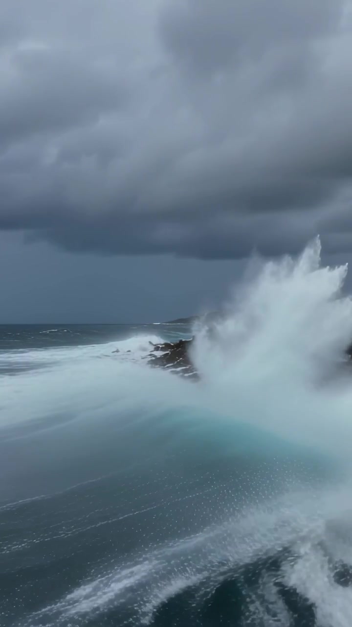Vertical video: Pushing swell driving waves crashing at stormy rocky coast sending spray and foam