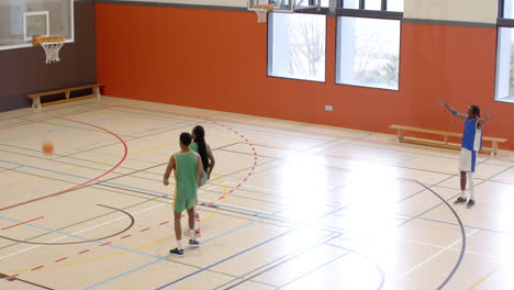 multiracial male basketball players in gym with male coach walking and observing game