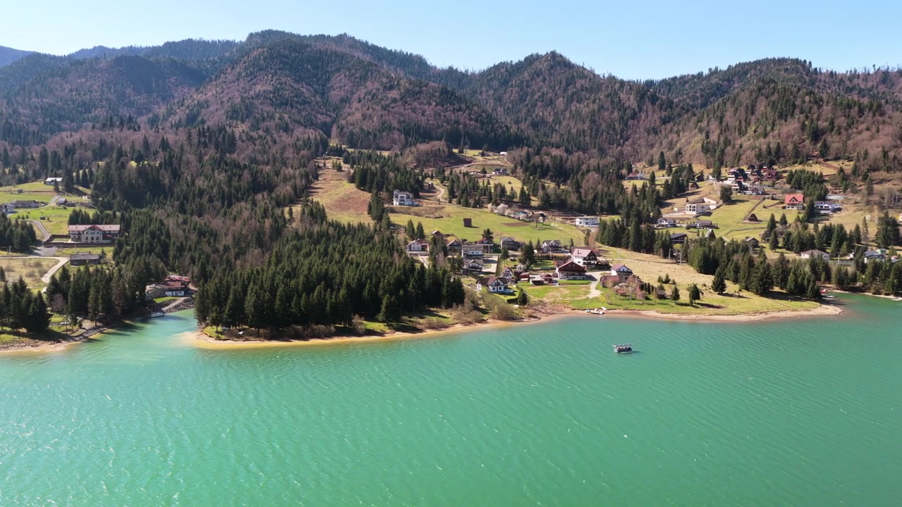 Veduta aerea con drone che mostra il lago Colibita e le colline circostanti con case sparse e foresta, in Romania