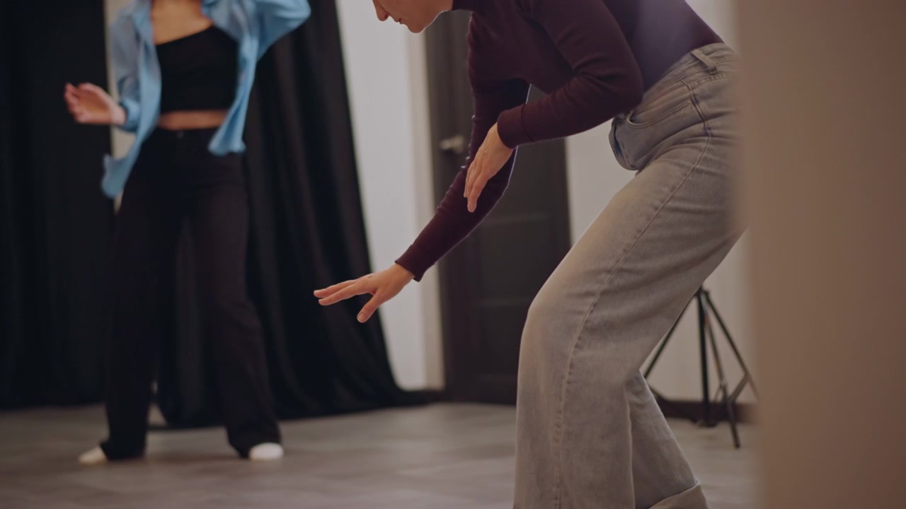 Instructor guiando a estudiante a través del movimiento, estudiante de danza practica pasos firmes mientras el instructor ofrece corrección directa, iluminación suave de estudio, grupo concentrado observando al fondo, deliberado