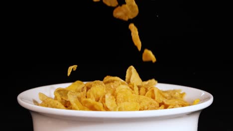 cornflakes cascade into a white bowl, set against a stark black background, creating a dynamic and visually striking scene