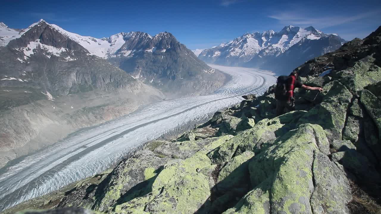 Hiker hiking above the Aletsch glacier in the Swiss Alps, view up glacier