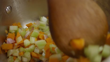 Stirring vegetable mix inside cooking pot with a wooden spoon