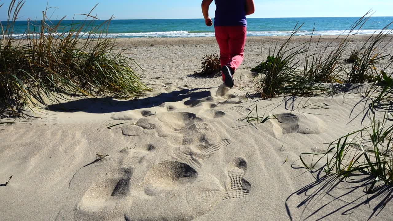 La donna corre sulle dune sabbiose verso il mare. Movimento rallentato