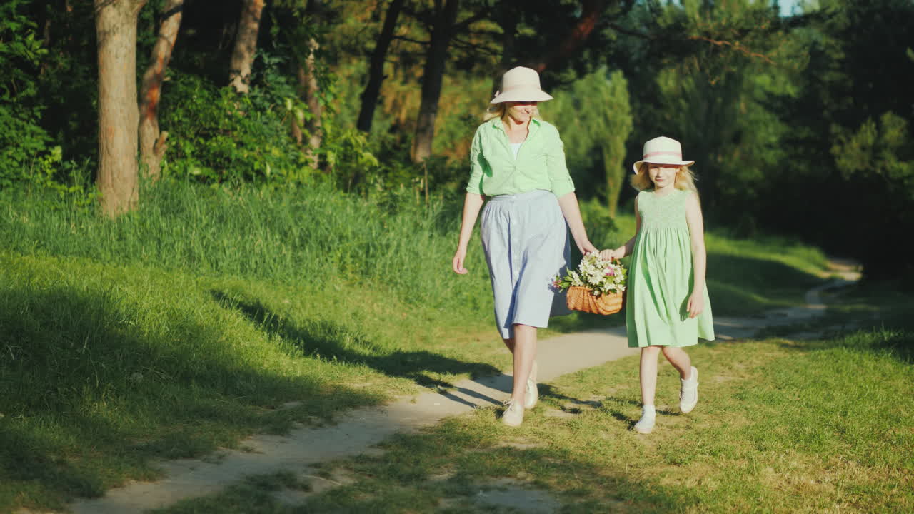 мама и дочь идут по тропинке в лесу, неся корзину с полевыми цветами happy par