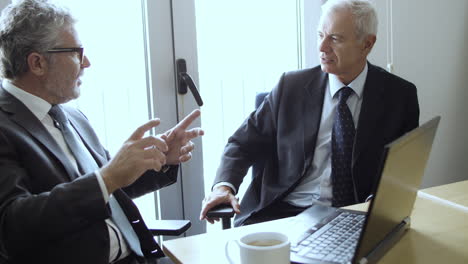 two serious mature businessmen sitting at laptop