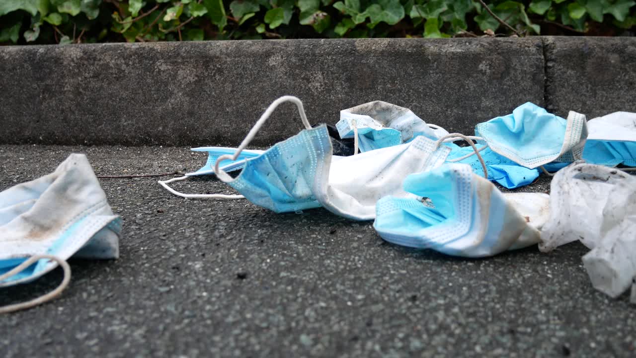 거리 보도에서 바람에 쓰레기를 날리는 더럽고 버려진 코로나 바이러스 마스크 돌리 느린 근접 촬영 오른쪽