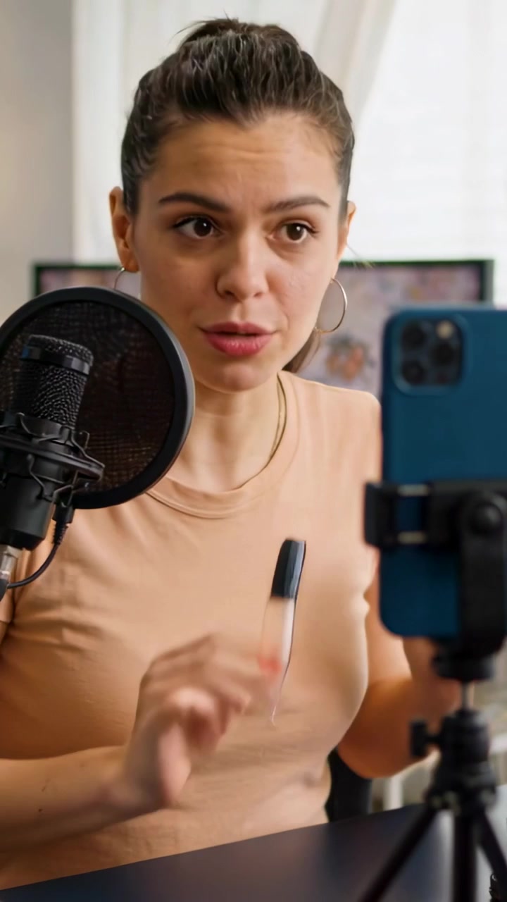 Vertical video: Recording host in beige top talking into phone in studio by mic showing product