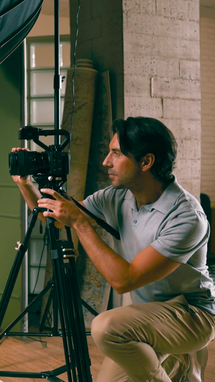 Videomaker che regola la telecamera su un treppiede in studio