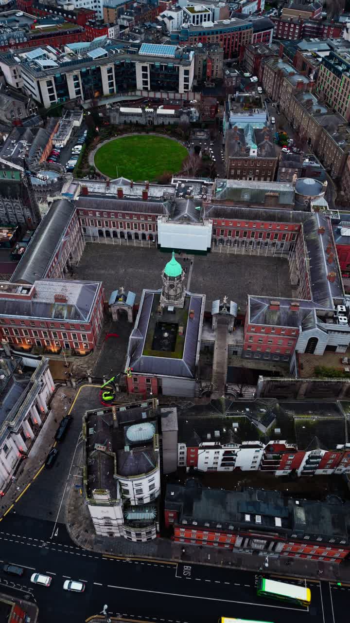 Drone shot over Dublin castle in the city centre in Ireland with busy streets below with cars and buses and tourists walking around in Irish cityscape on cloudy overcast day in winter