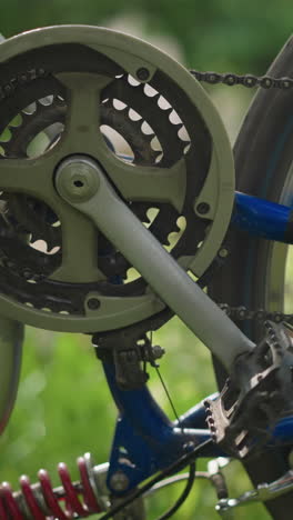 primer plano de la rueda trasera de la bicicleta y el sistema de engranajes mientras la rueda gira lentamente, la cadena y el engranaje están en foco, mientras que el fondo está borroso, con un indicio de alguien caminando