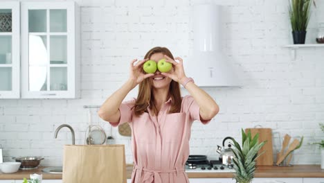 smiling girl in the kitchen holds green apples in her hands and closes her eyes with them. healthy eating concept. woman on a diet