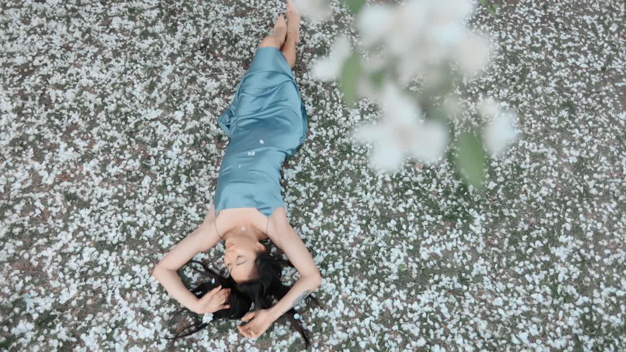 Woman in a blue silk dress lying in a spring garden