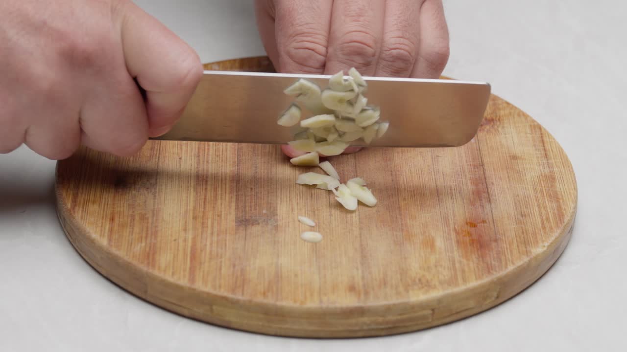 Primo piano di mani che tagliano aglio fresco su un tagliere di legno per la preparazione della cottura