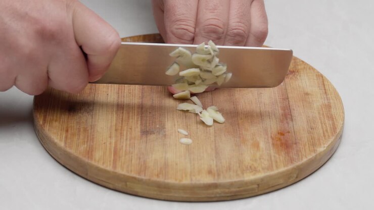 Primo piano di mani che tagliano aglio fresco su un tagliere di legno per la preparazione della cottura