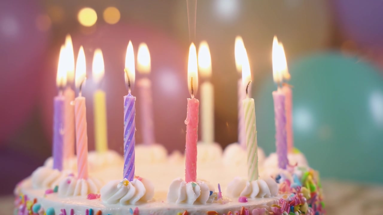 Torta di compleanno vivace guarnita con candeline accese e codette colorate