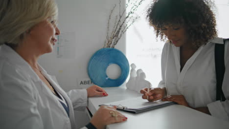 clinic patient signing agreement at counter closeup. woman receptionist assist