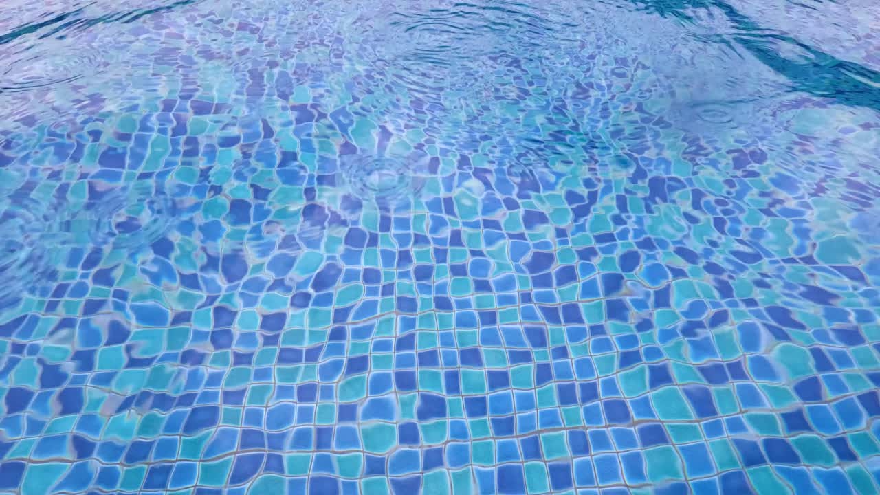 Vandkrusninger på blå flisebelagt swimmingpool under regn