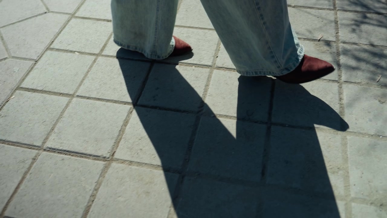 Pretty red heels on sunlit pavement, closeup legs in light trousers casting long shadows, textured tile grid, slow stylish stride, street model showcasing shoe detail, candid urban mood