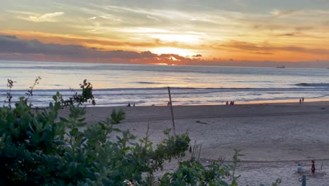 siluetas de personas caminando en la playa de arena y surfistas al fondo del atardecer en la costa atlántica de portugal
