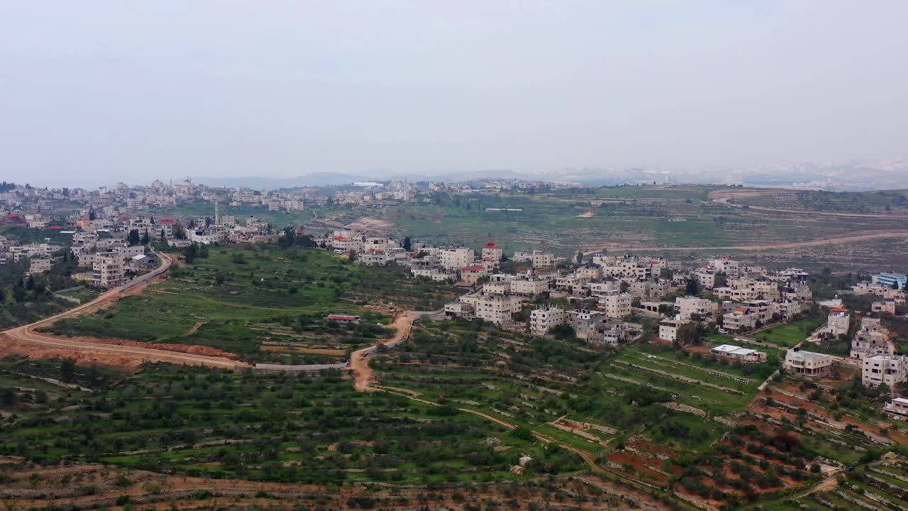 Aerial view of a hillside village with terraced fields under an overcast sky