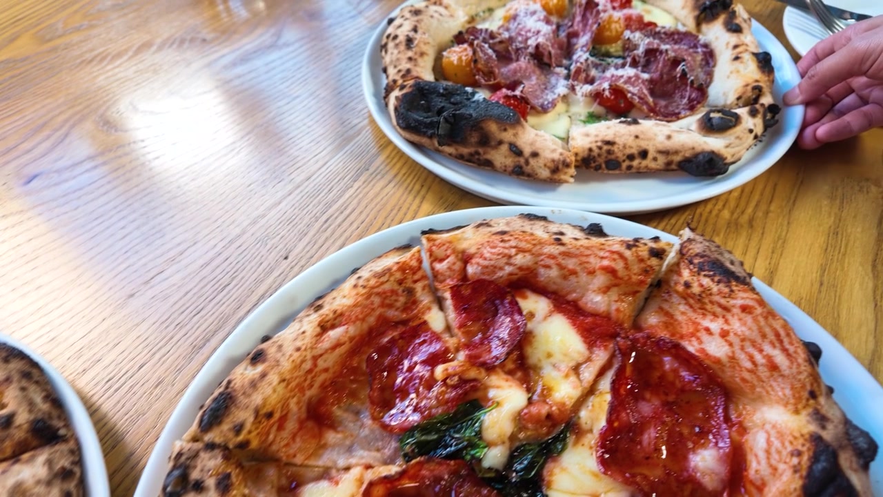 Primo piano di varie pizze a lievitazione naturale servite su un tavolo di legno in un ristorante luminoso