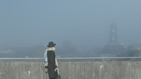 woman walks across the rooftop looking at city watch tower in misty sunny day