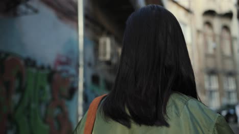 back view on the stylish young girl walking the slums street with graffity, then turning to the camera and smiling joyfully