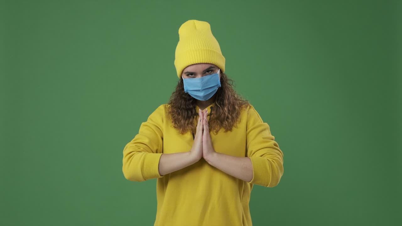 mujer con máscara protectora y dando varios gestos de saludos con la mano sobre la pantalla verde