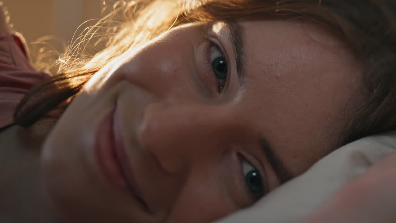 en primer plano una chica adormecida despertando temprano en la mañana. una mujer muy sonriente descansando en la cama