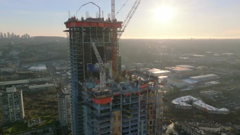 development site of tall apartment buildings with cranes at work on the rooftop at sunset in burnaby, british columbia, canada