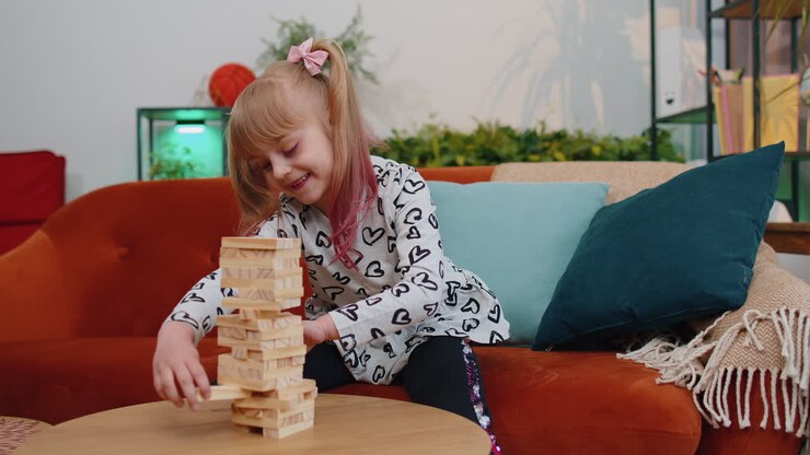 Funny happy one teenage kid girl play wooden tower blocks bricks game at home in modern living room