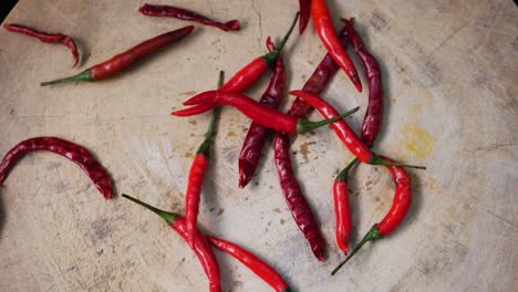 Slow-Motion-of-Red-Chili-Peppers-Drops-Down-Into-Cutting-Board,-Top-Down