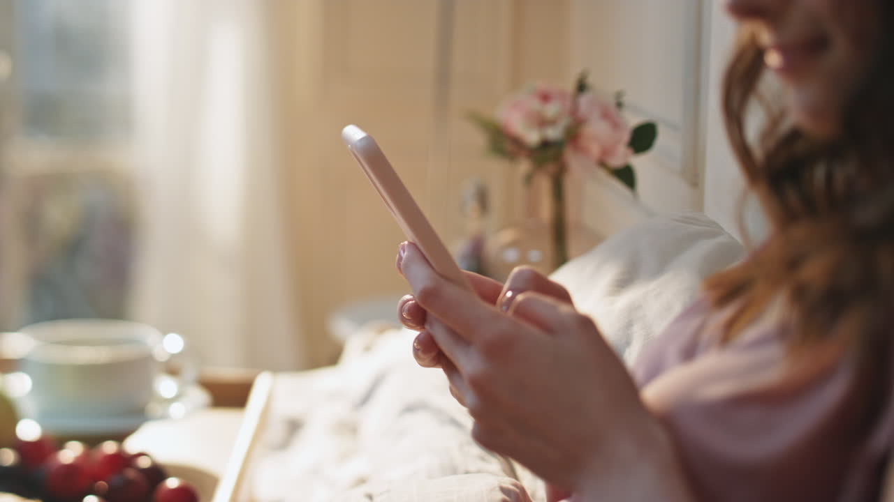 Primo piano di una bella ragazza che digita sul telefono cellulare in una casa accogliente. Mani che tengono lo smartphone.
