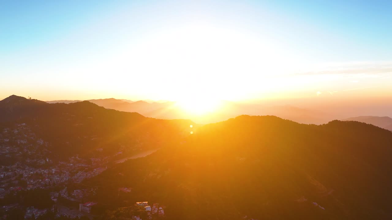 Aerial drone shot of soft morning light spreading over the forested hills of Nainital during sunrise.