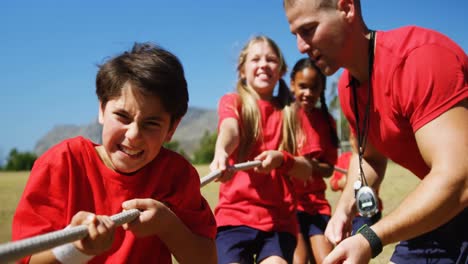 entrenador ayudando a los niños en el tira y afloja durante el entrenamiento de cursos de obstáculos