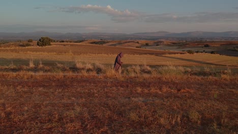 A-profile-shot-following-a-monk-walking-towards-right-on-a-brown-fields