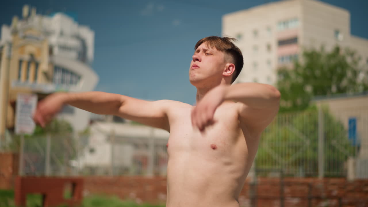 한 남자가 야외에서 섀도 복싱을 하고, 한 사람이 정오의 햇볕이 내리쬐는 마당에서 섀도 복싱을 합니다. 웃통을 벗은 백인 남성이 햇볕이 잘 드는 마당에서 활기차게 섀도 복싱을 하고 있어요.