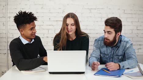 grupo diverso de jóvenes empresarios discutiendo negocios usando computadora portátil en la oficina. dos hombres están discutiendo mientras jóvenes