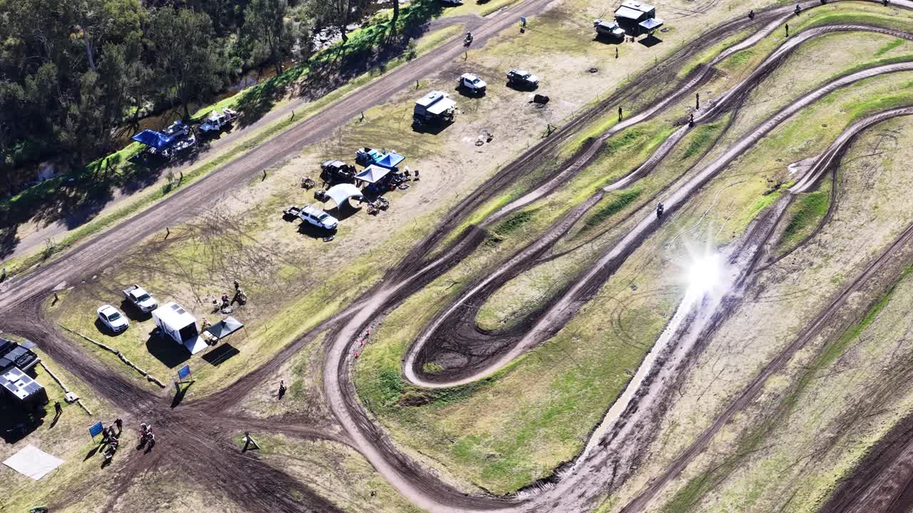 Drone captures motocross track, vehicles, and tents under bright daylight at rural outdoor park