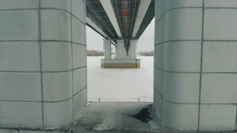 grey bridge support construction in white frozen river