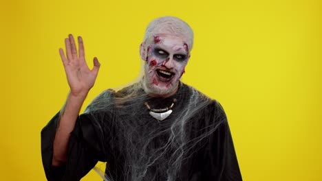 creepy halloween zombie man smiling friendly waving hands gesturing hello or goodbye, welcoming