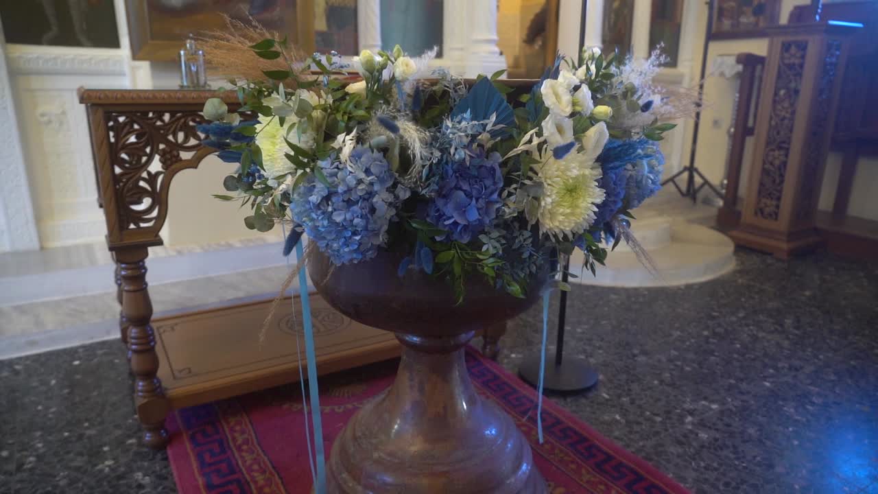 Cinematic slow-motion shot of a baptismal font decorated with blue flowers inside a church, highlighting sacred details, warm light, and a serene, spiritual atmosphere