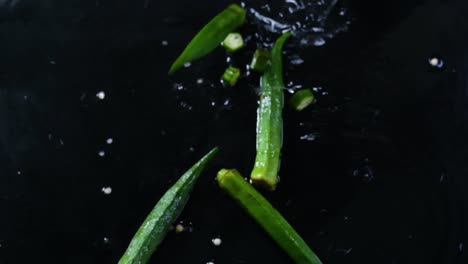 slow motion shot of chopped green chili pieces falling among other chili peppers in a puddle of water