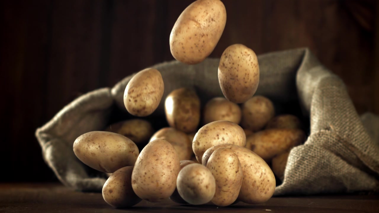 Rallentatore di patate crude che cadono su una superficie di legno rustica